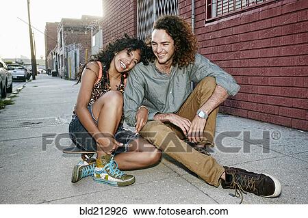 Couple sitting on skateboard on city street View Large Photo Image Stock Photograph - Couple sitting on skateboard on city street. Fotosearch