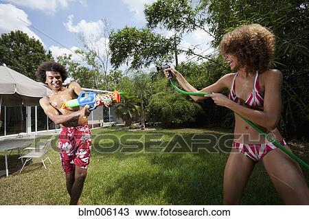 Couple squirting each other with water in backyard View Large Photo Image Stock Image - Couple squirting each other with water in backyard. Fotosearch