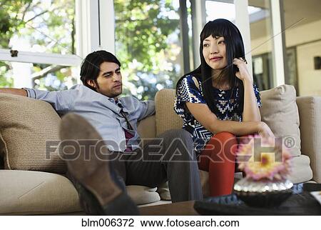 Couple unwinding on sofa in living room View Large Photo Image Stock Image - Couple unwinding on sofa in living room. Fotosearch
