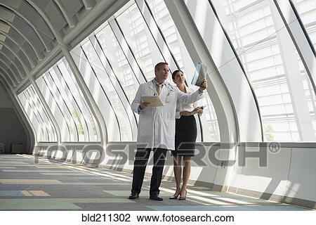 Stock Image - Doctor and businesswoman talking in corridor. Fotosearch