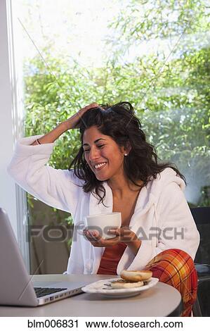 Stock Image - Ecuadorian woman drinking coffee and looking at laptop. Fotosearch