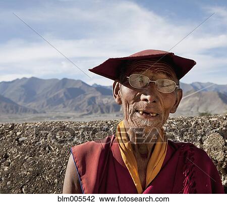 Stock Image - Elderly Tibetan monk in eyeglasses and hat. Fotosearch