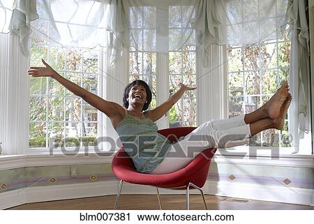 Stock Image - Excited Black woman sitting in chair. Fotosearch