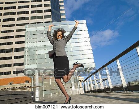Stock Image - Excited Caucasian Businesswoman standing on one leg in city. Fotosearch