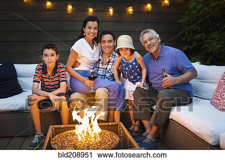 Stock Image - Family smiling around fire pit outdoors. Fotosearch