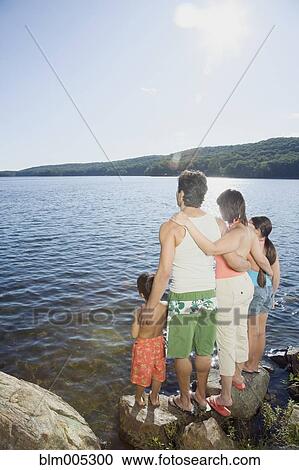 Stock Image - Family standing by lake. Fotosearch