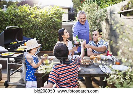Stock Image - Family toasting each other at table outdoors. Fotosearch