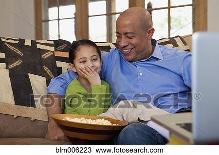 Stock Image - Father and daughter eating popcorn. Fotosearch