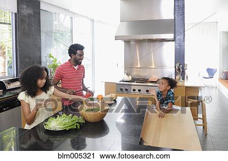 Stock Image - Father and daughters preparing food in kitchen. Fotosearch