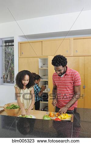 Stock Image - Father and daughters preparing food in kitchen. Fotosearch