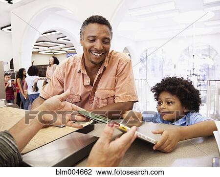 Stock Image - Father and son checking out books from library. Fotosearch