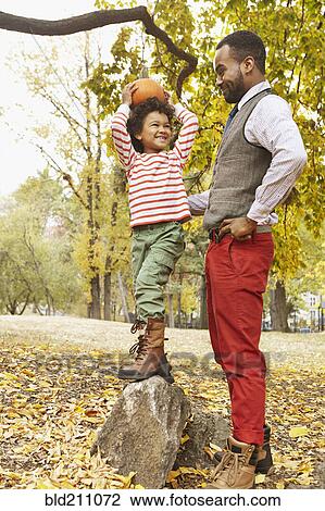 Stock Image - Father and son holding pumpkin in park. Fotosearch
