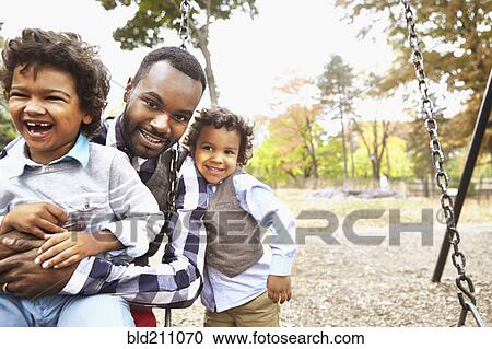 Stock Image - Father and sons playing together in park. Fotosearch