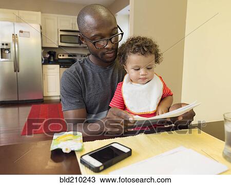 Stock Image - Father and toddler son sitting at table. Fotosearch