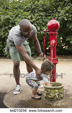 Stock Photograph - Father and toddler son using water fountain in park. Fotosearch