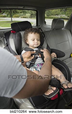 Picture - Father buckling toddler son into car seat. Fotosearch