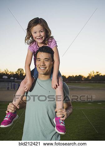 Stock Image - Father carrying daughter on shoulders in park. Fotosearch