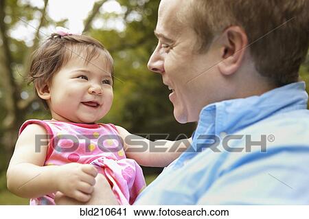 Stock Image - Father holding baby girl in park. Fotosearch
