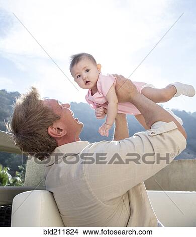 Picture - Father holding baby girl on sofa. Fotosearch
