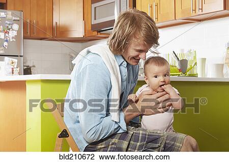 Stock Image - Father holding baby in kitchen. Fotosearch