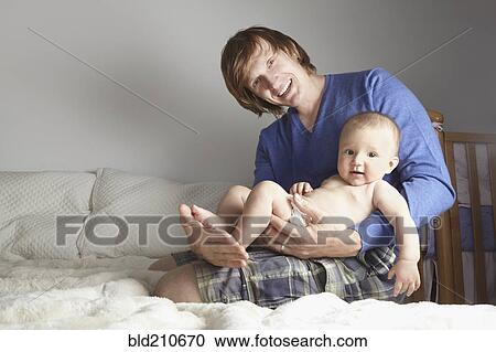 Stock Image - Father holding baby on bed. Fotosearch