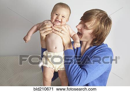 Stock Image - Father holding baby on bed. Fotosearch