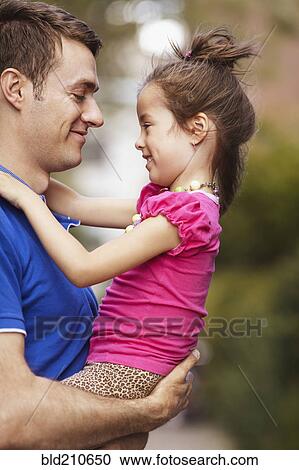 Stock Image - Father holding daughter on city street. Fotosearch