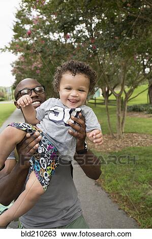 Stock Image - Father holding toddler son in park. Fotosearch