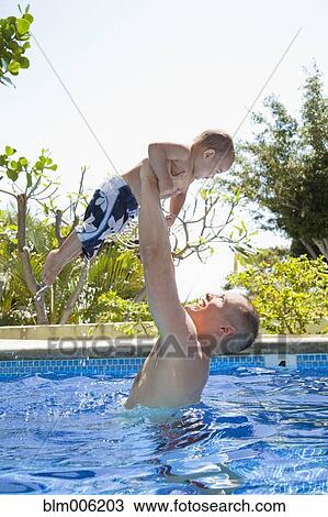 Stock Image - Father lifting son in swimming pool. Fotosearch