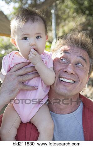 Stock Image - Father playing with baby girl outdoors. Fotosearch