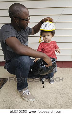 Stock Image - Father putting helmet on toddler son. Fotosearch