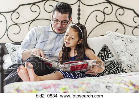 Picture - Father reading to daughter on bed. Fotosearch