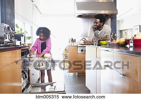 Stock Photography - Father watching daughter loading dishwasher. Fotosearch