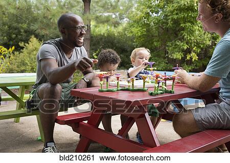 Stock Image - Fathers and toddler sons playing at picnic table. Fotosearch