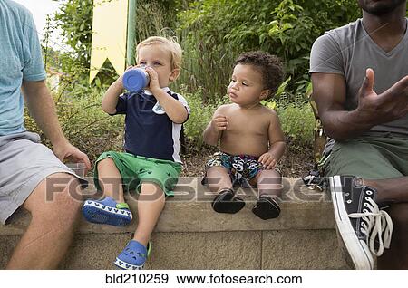 Fathers and toddler sons sitting together in park View Large Photo Image Stock Photo - Fathers and toddler sons sitting together in park. Fotosearch