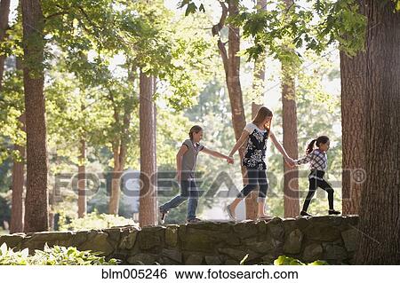 Stock Photograph - Friends holding hands and walking on stone wall. Fotosearch