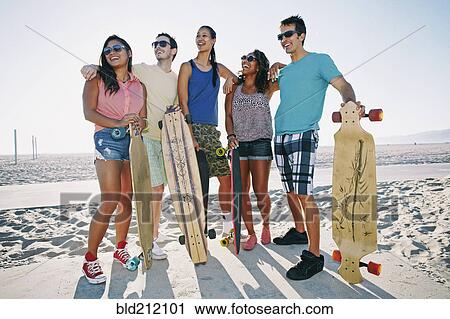Stock Image - Friends holding longboards on beach. Fotosearch
