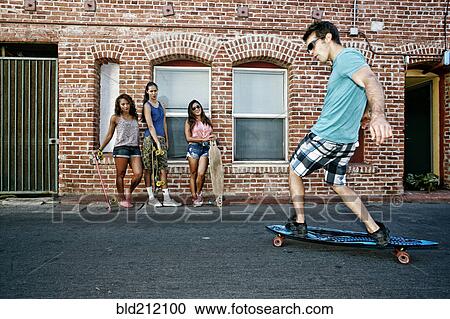 Stock Image - Friends riding longboards on city street. Fotosearch