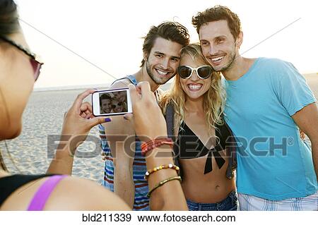 Stock Photo - Friends taking pictures together on beach. Fotosearch