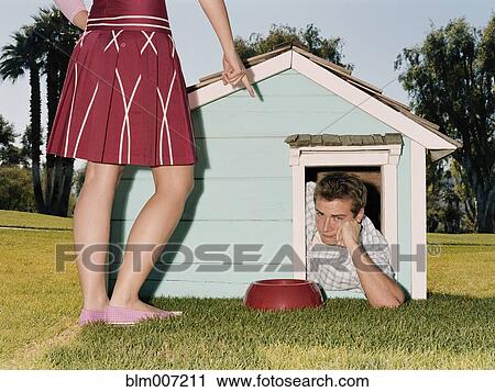 Stock Image - Frustrated man laying in doghouse. Fotosearch