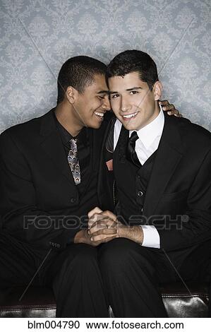 Stock Image - Gay couple hugging on sofa. Fotosearch