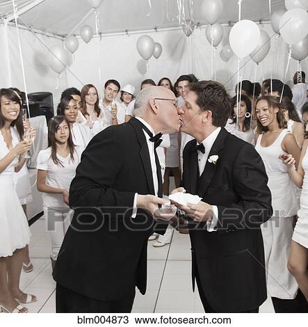 Stock Image - Gay married couple eating cake at wedding reception. Fotosearch