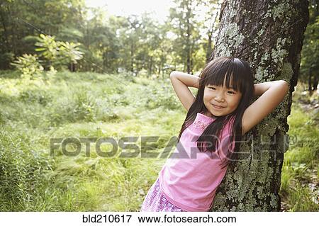 Stock Photo - Girl leaning against tree outdoors. Fotosearch