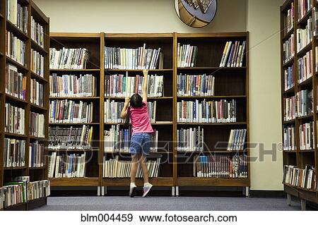 Girl reaching for book on library shelf View Large Photo Image Stock Photo - Girl reaching for book on library shelf. Fotosearch