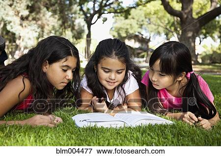 Stock Photo - Girls laying in grass reading book in park. Fotosearch