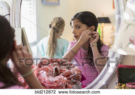 Stock Image - Girls putting on earrings in bedroom. Fotosearch