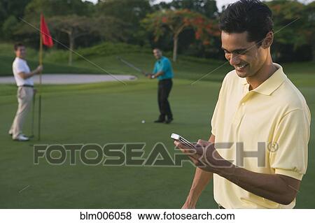 Stock Photo - Golfer text messaging on cell phone. Fotosearch