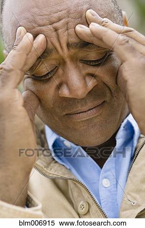 Stock Photography - Grimacing mixed race man rubbing forehead. Fotosearch