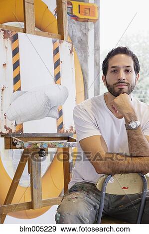 Stock Photo - Hispanic artist sitting near canvas. Fotosearch
