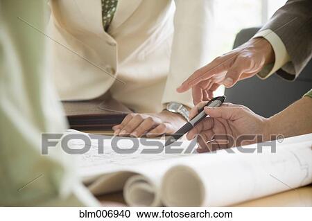Stock Image - Hispanic business people looking at blueprints. Fotosearch